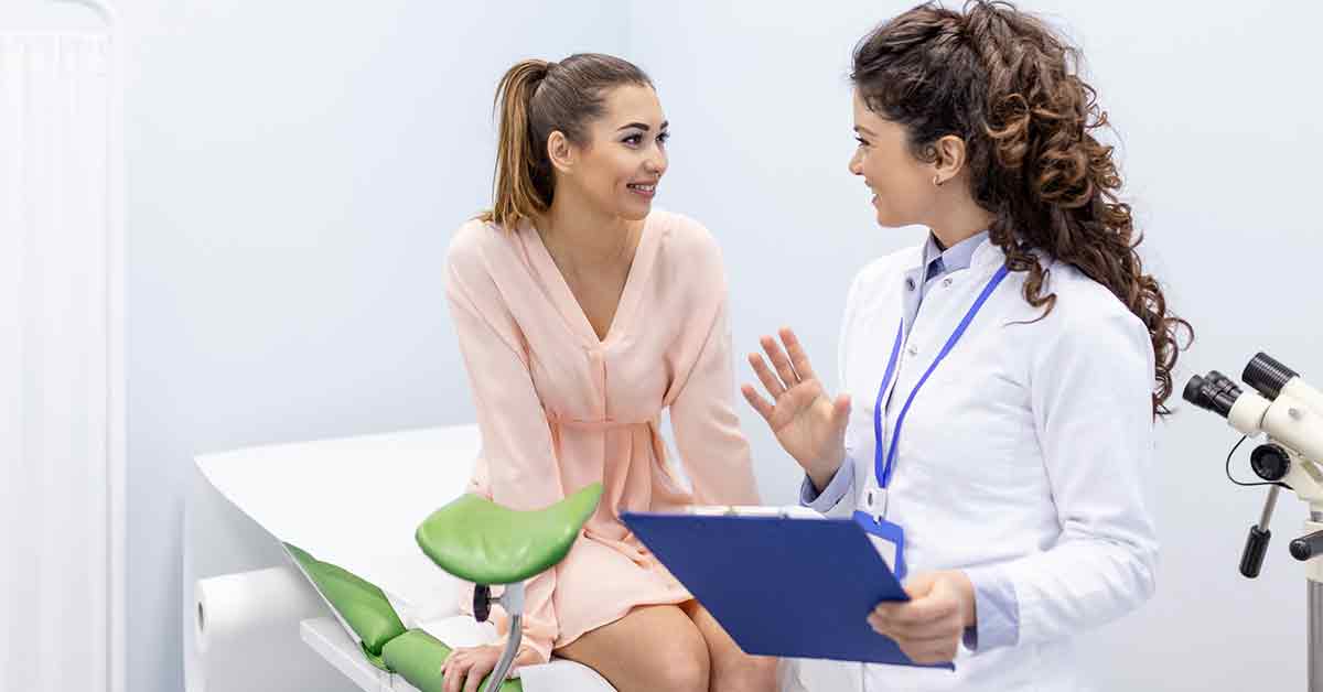 Woman sitting on an exam table talking to her GYN