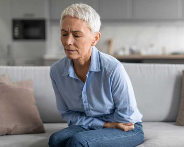Senior Woman Having Stomachache Sitting On Sofa At Home