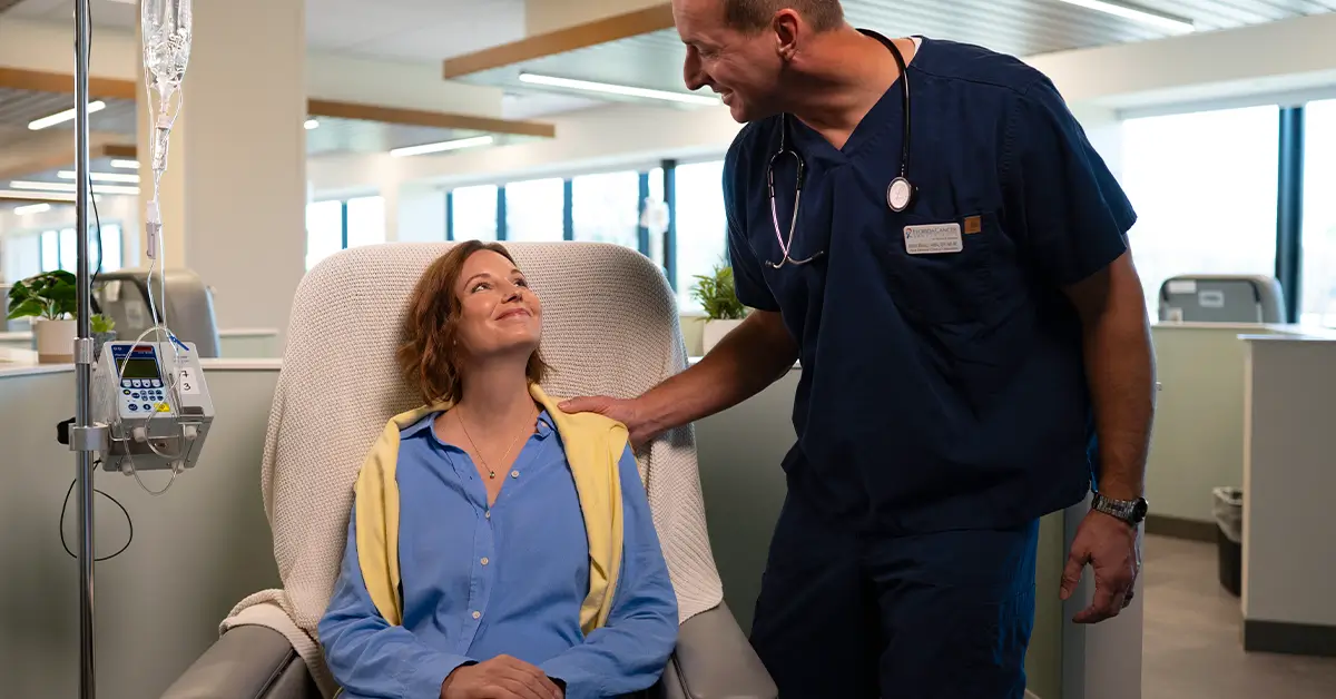 A cancer patient receiving infusion therapy while a care team member offers support
