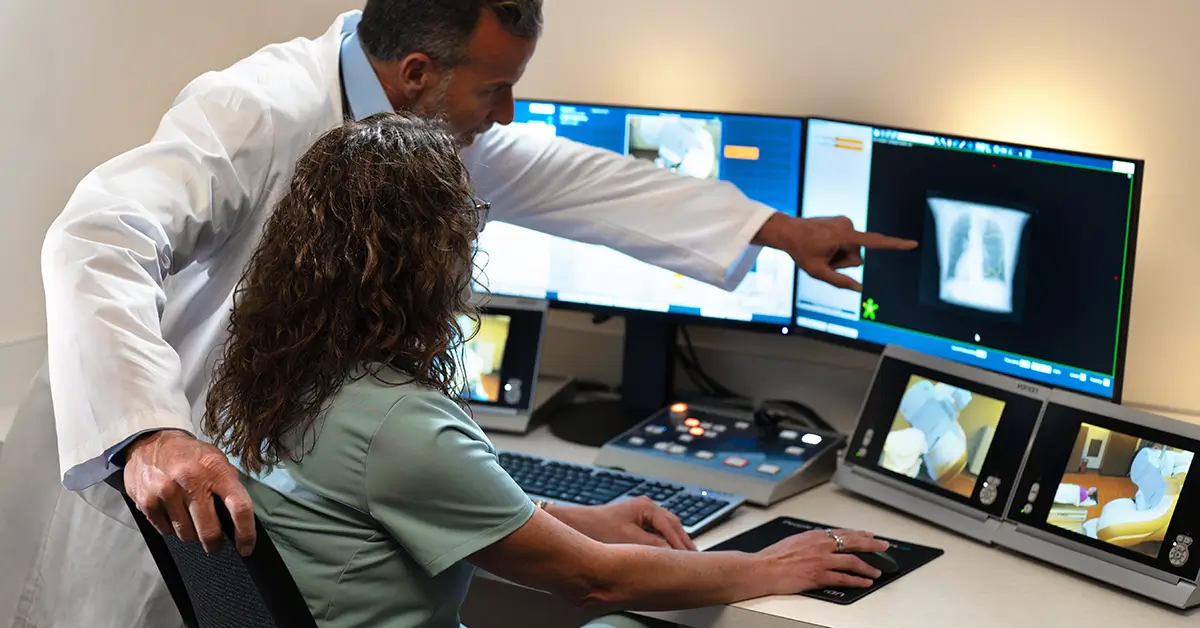 Two oncology specialists reviewing cancer imaging scans on multiple monitors