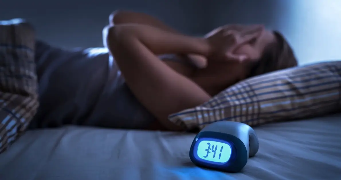 Woman lying awake in bed at 3:41 a.m. with a glowing alarm clock in the foreground — sleep problems affect 30 to 50% of cancer patients. Florida Cancer Specialists & Research Institute.