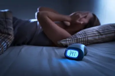 Woman lying awake in bed at 3:41 a.m. with a glowing alarm clock in the foreground — sleep problems affect 30 to 50% of cancer patients. Florida Cancer Specialists & Research Institute.